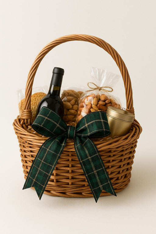 Wicker gift basket with wine bottle, snacks, and a plaid bow on a white background