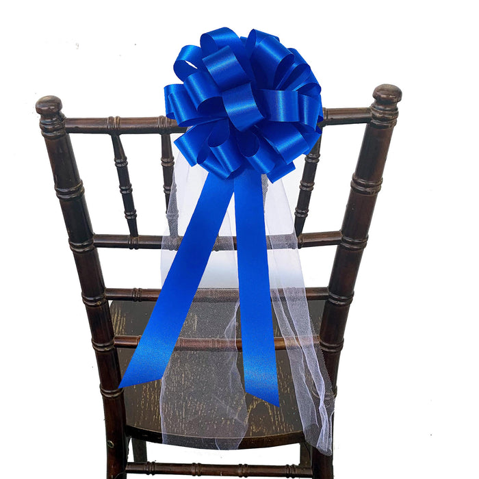 A cornflowerl blue satin bow with a long matching ribbon and a sheer white tulle undersheet, attached to the back of a dark brown wooden chair against a white background.