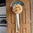 A large decorative bow made from gold and white ribbon is hanging on a brown wooden front door with a glass arched window at the top.
