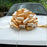 A large decorative gift bow made from wide gold and ivory satin ribbon, tied on the hood of a white car with a hedge visible in the background.